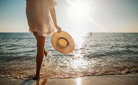 woman with sun hat on beach with her feet in the water