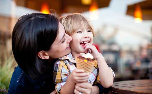 mom snuggles child holding an ice cream cone and smiling